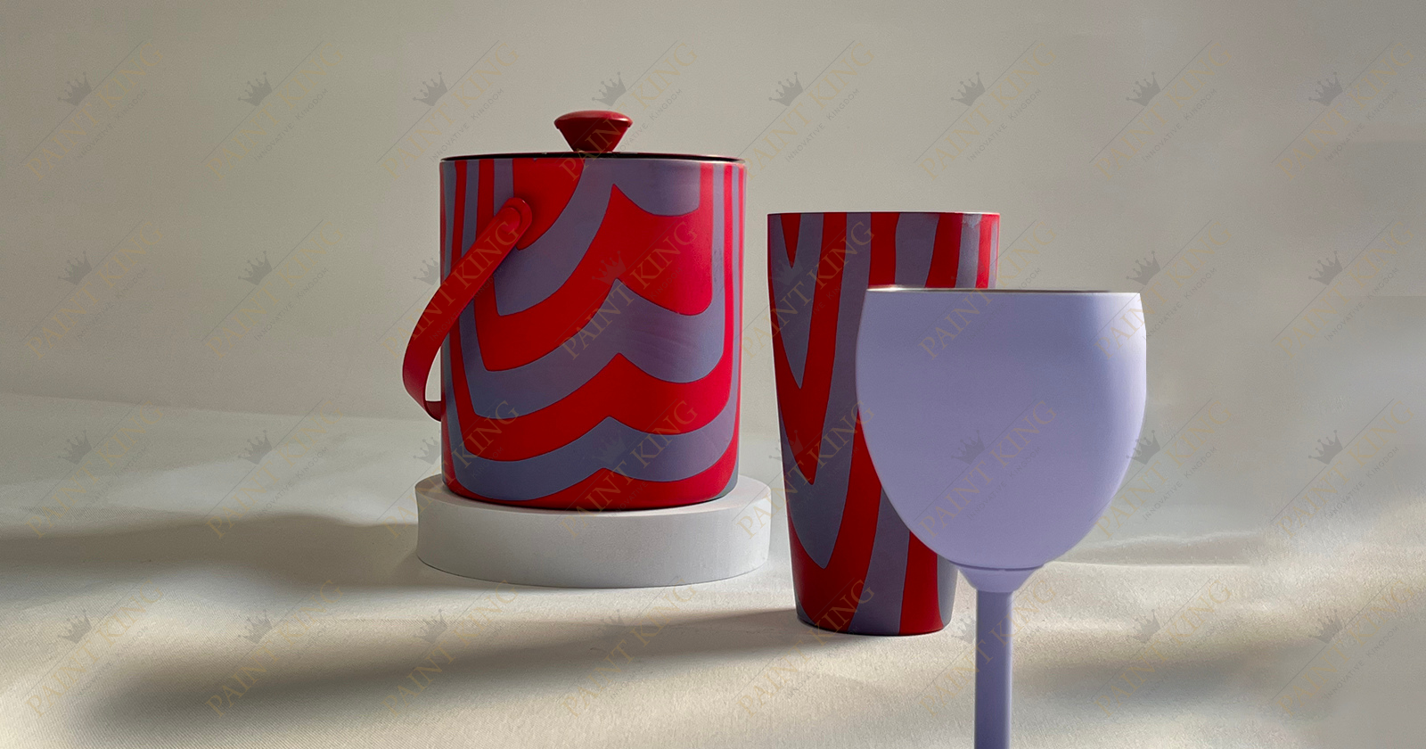 A photo of a collection of barware, showcasing the intricate details of spray-painted and hydrographic-printed designs on a cylindrical ice bucket with a handle, a tall cocktail shaker, and a wine glass.