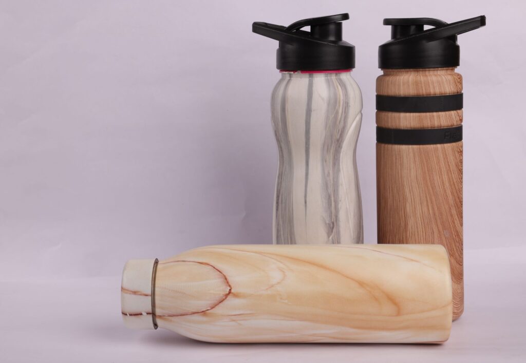 Three hydrographic printed bottles, one with a white and gray marble pattern, one with a brown wood grain pattern, and one with a light brown wood grain pattern.